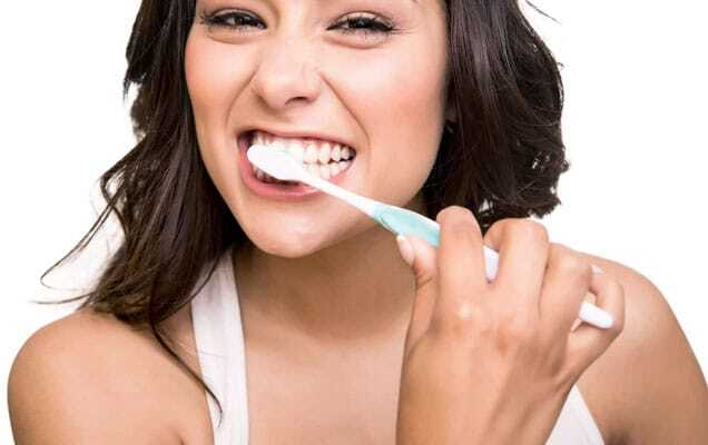 Woman brushing her teeth with a toothbrush and smiling brightly.
