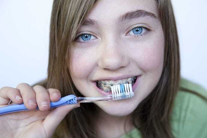 Young girl brushing teeth with orthodontic braces and a blue toothbrush.
