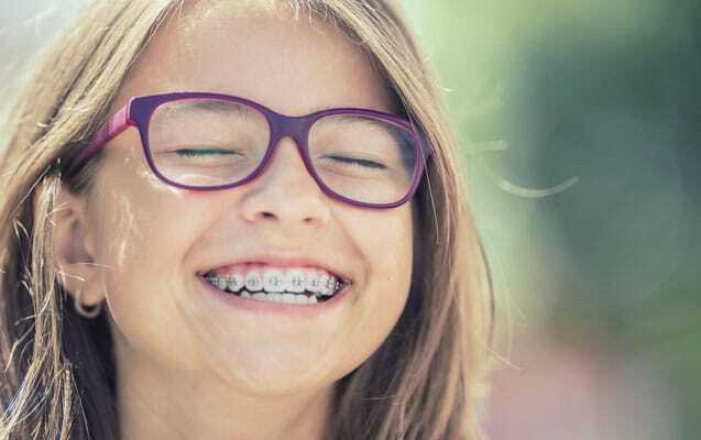 Smiling girl wearing purple glasses and braces showing her beautiful healthy teeth.