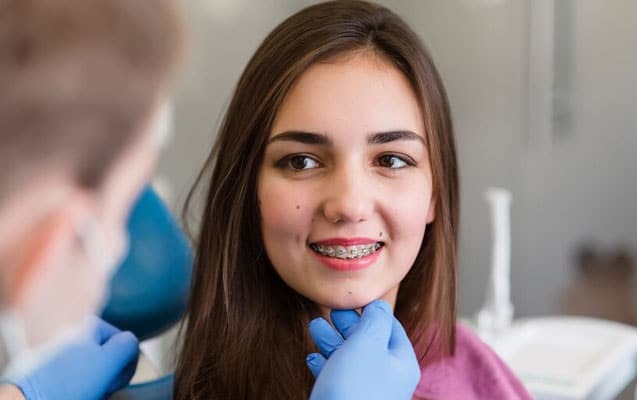 Young female patient smiling with pink braces during dental consultation in Woodbury.