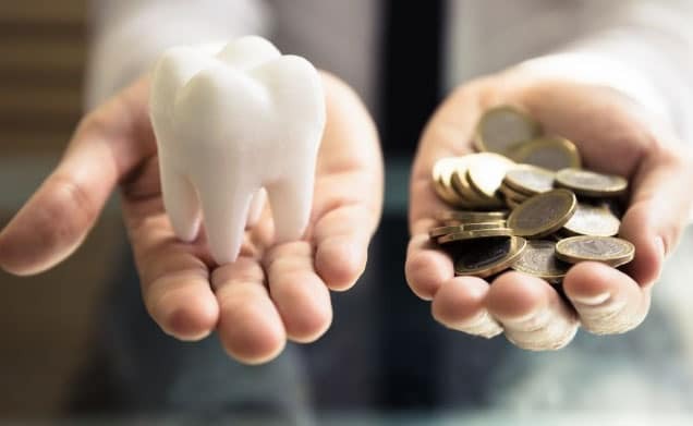 Person comparing tooth model and coins, symbolizing dental treatment costs.