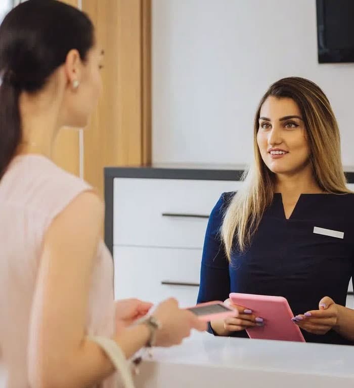 Receptionist at dental office desk smiling while greeting patient.