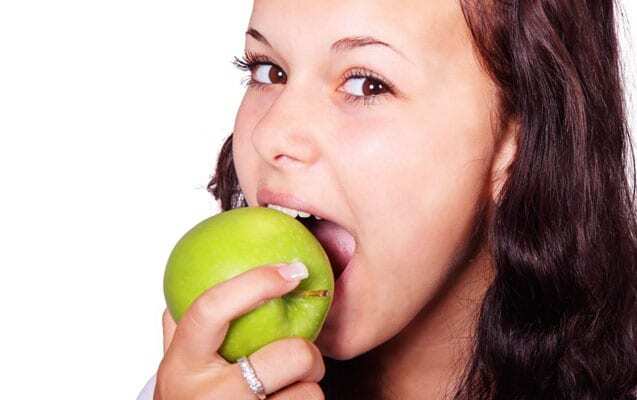 Woman biting into a green apple, demonstrating healthy eating habits for dental health.