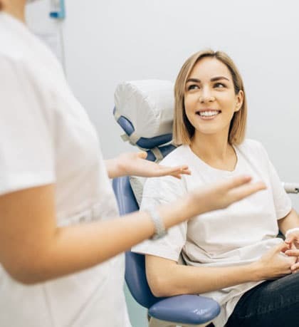 Smiling patient sitting in dental chair while dentist explains treatment options.