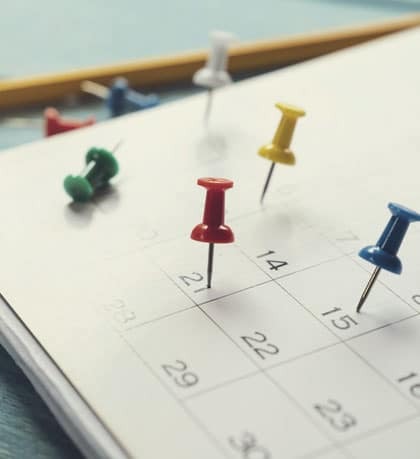 Colorful pushpins marking appointment dates on a dental practice calendar for scheduling.