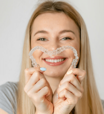 Young woman holding clear Invisalign aligners and smiling, showing teeth whitening results in Woodbury.