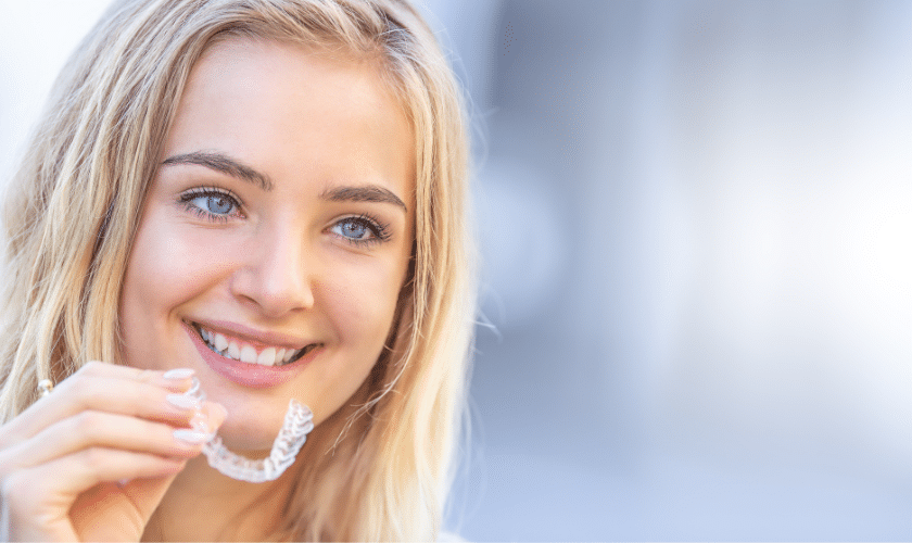 Young woman smiling while holding clear Invisalign aligner tray.