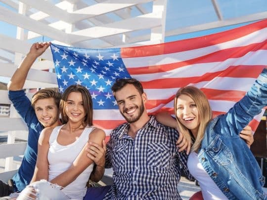 Happy family celebrating Independence Day with American flag outdoors.