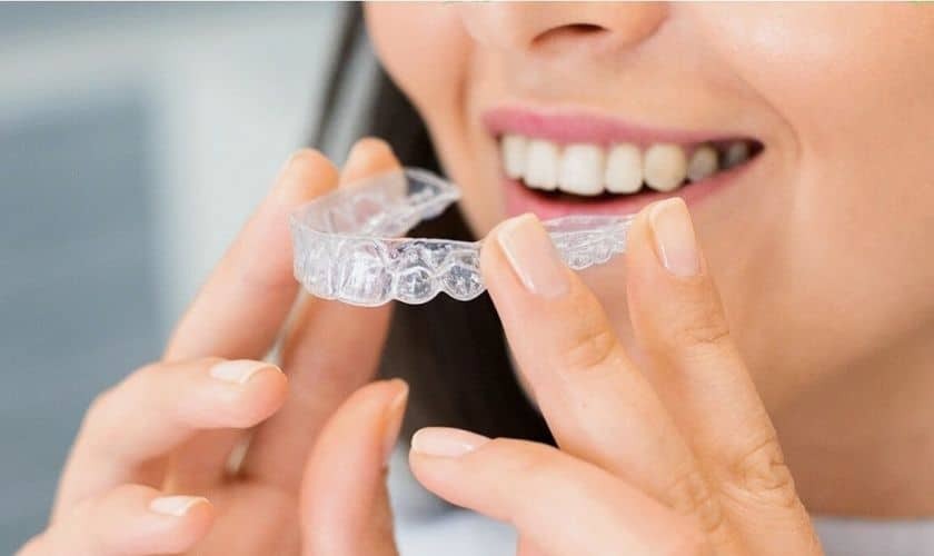 Woman holding clear Invisalign aligner tray while smiling to show teeth straightening results.