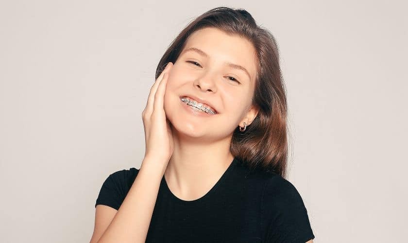 Smiling young woman with metal braces showing successful orthodontic treatment results.