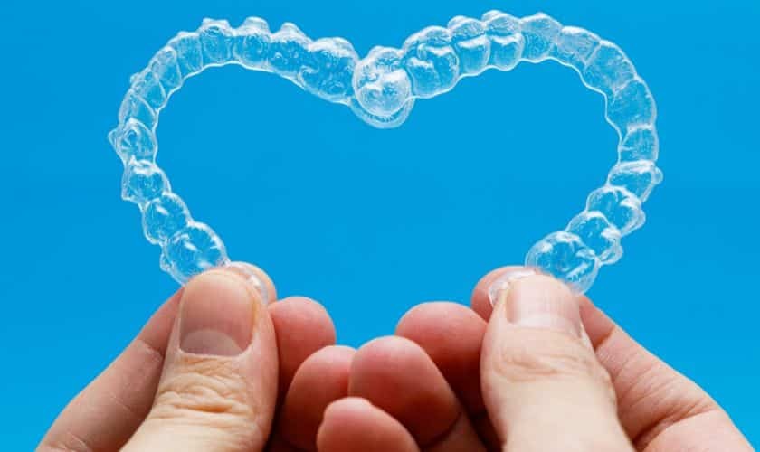 Hands holding a heart-shaped bubble against a blue background representing dental care and smile health.