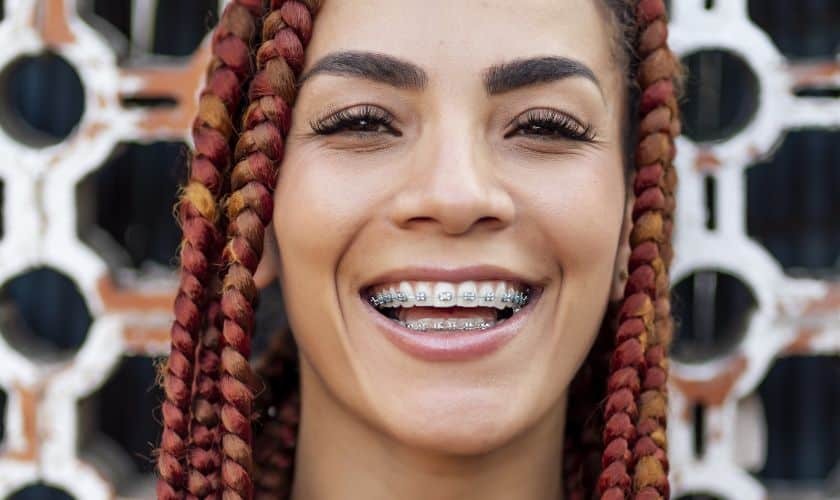 Young woman with red braids smiling confidently while wearing metal dental braces.