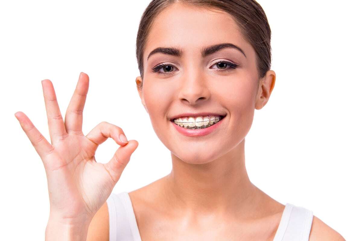 Smiling woman with metal braces giving an OK hand gesture, promoting orthodontic retention care.