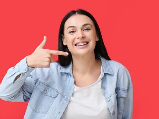 Young woman smiling confidently with bright teeth against red background.