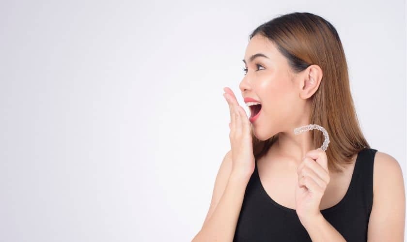 Woman holding invisible aligner showing excitement about smile transformation results.