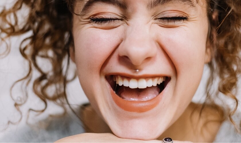 Woman with a bright, healthy smile showing white teeth and orange lipstick.