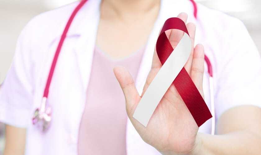 Healthcare provider holding red and white awareness ribbon for oral cancer prevention.