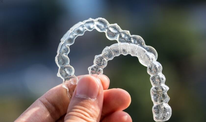 Clear Invisalign aligners held in hand, showing tooth-straightening treatment option.