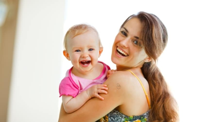 Happy mother holding smiling baby in pink shirt, representing family dental care.