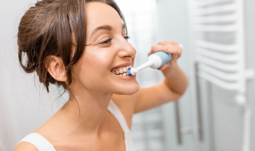 Woman brushing her teeth with an electric toothbrush in a bathroom setting.