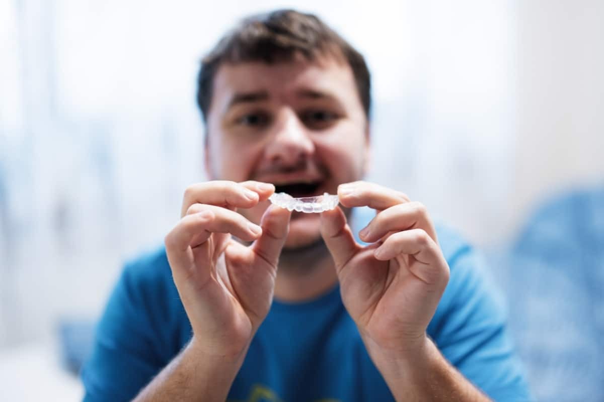 Man holding clear Invisalign aligner while smiling at camera.