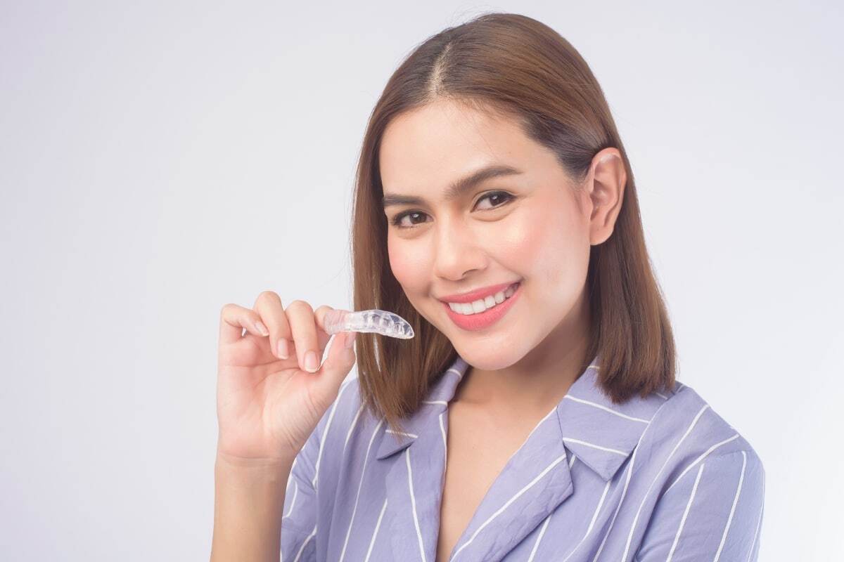 Woman holding clear Invisalign aligner tray and smiling to show dental results.