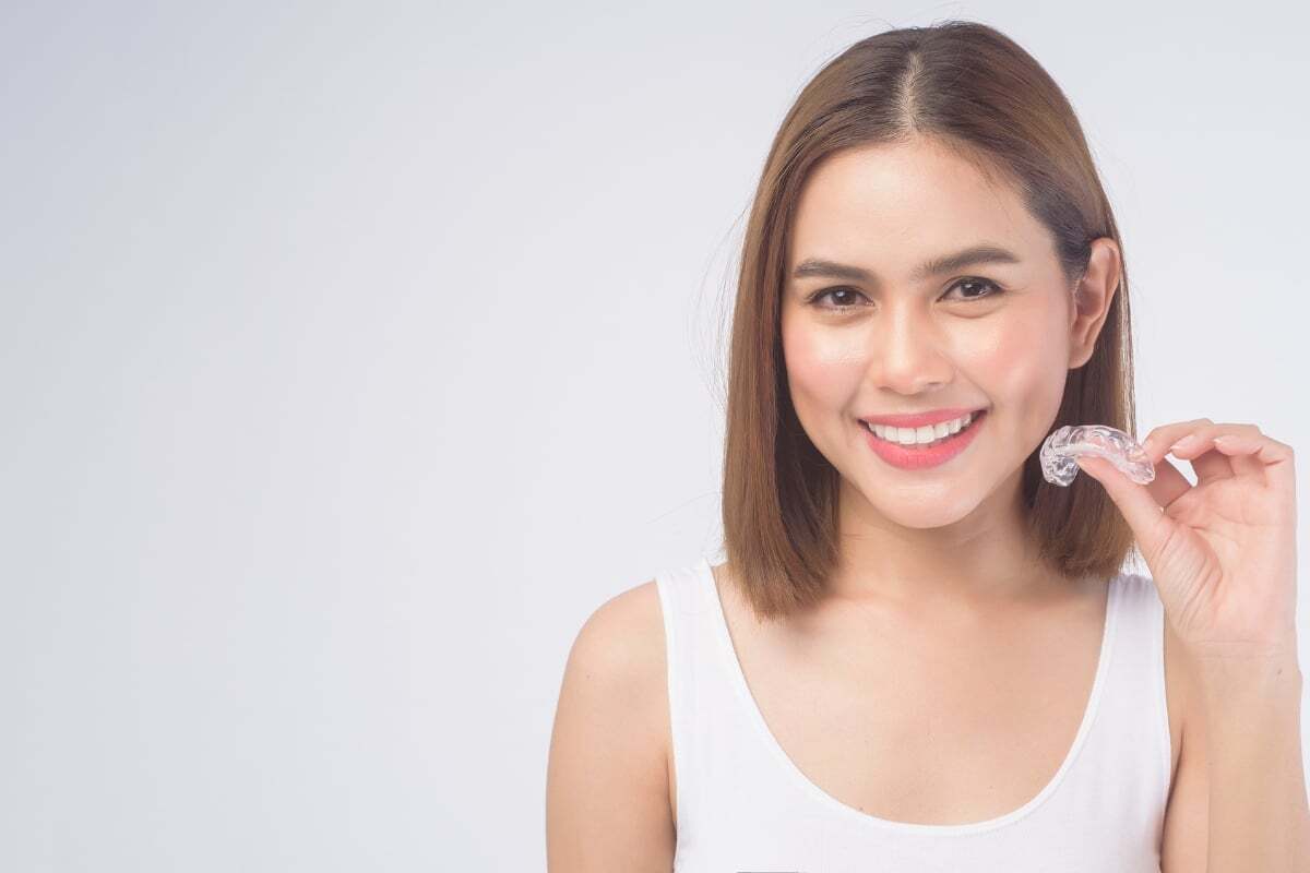 Woman holding clear Invisalign aligner while smiling, demonstrating orthodontic treatment option.