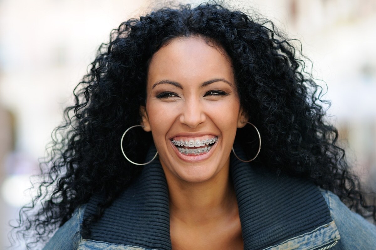 Woman with braces smiling, wearing hoop earrings and denim jacket.