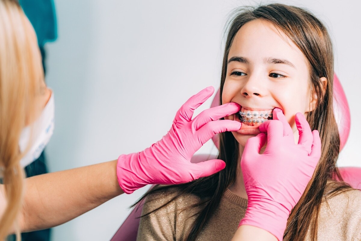 Orthodontist examining patient's metal braces during dental checkup.