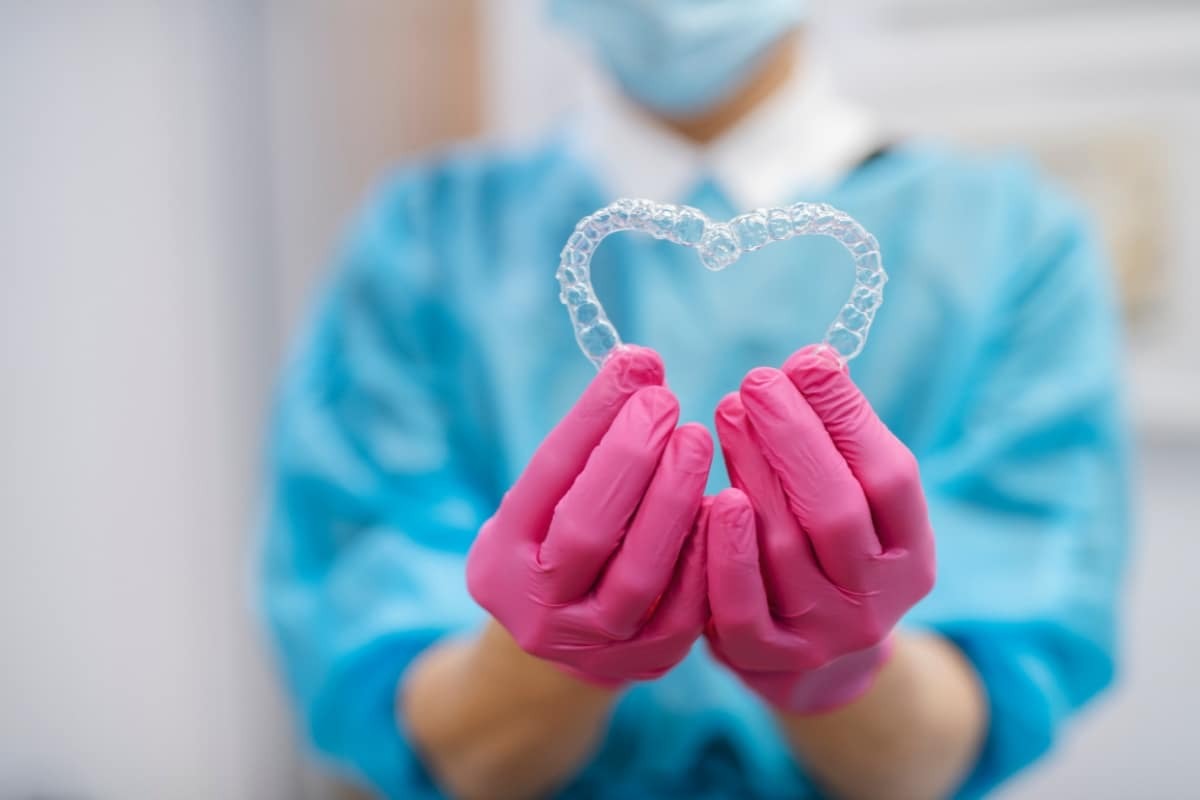 Healthcare professional holding clear orthodontic retainer in pink gloved hands, symbolizing dental care.