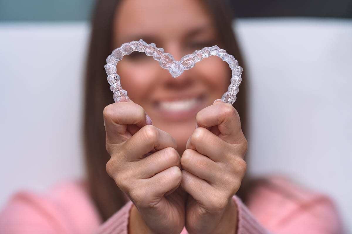 Girl holding clear Invisalign retainer shaped like a heart in front of her smiling face.