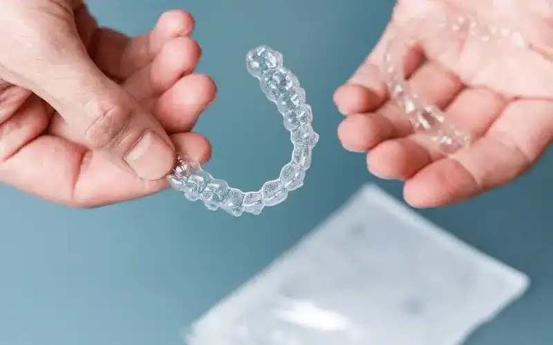 Person holding a clear Invisalign aligner tray against a blue background.