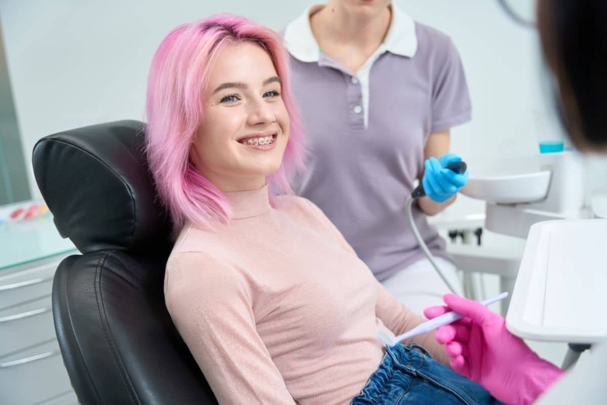 Young patient with pink hair smiling in dental chair during orthodontic consultation.