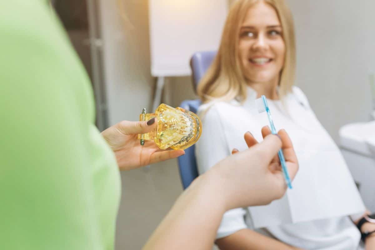 Orthodontist showing yellow dental retainer to smiling patient during consultation.