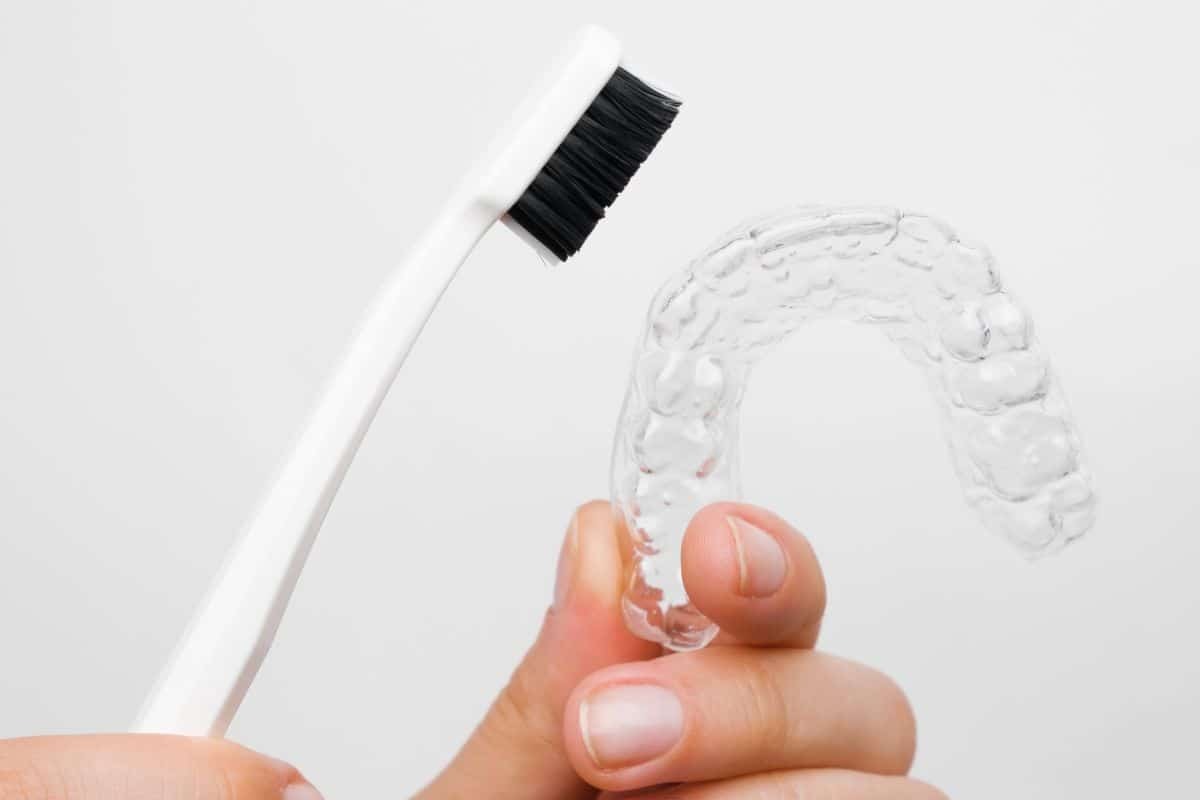 Invisalign aligner being cleaned with a soft-bristled toothbrush and paste.