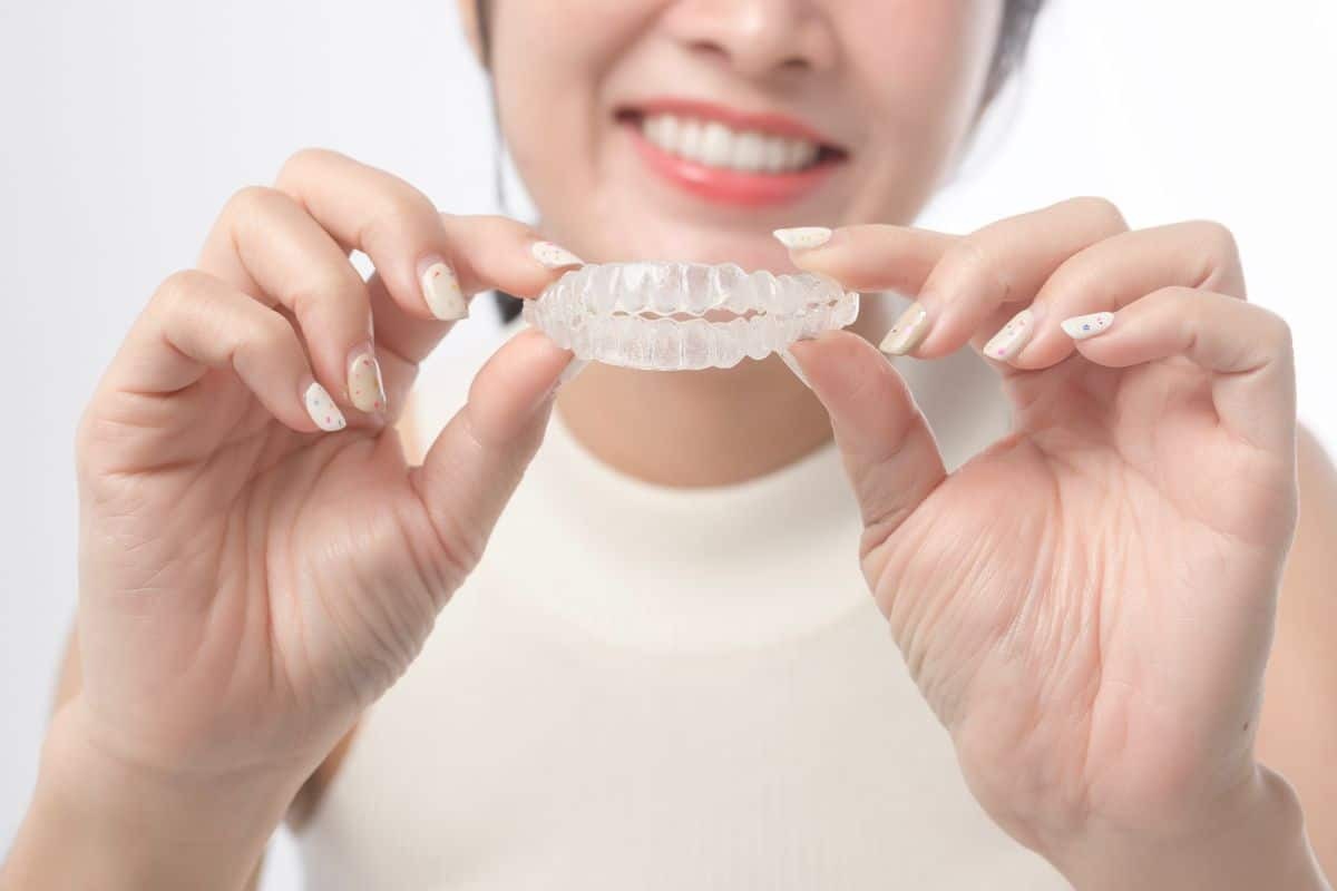 Woman holding clear Invisalign aligner tray, smiling at camera during orthodontic treatment.