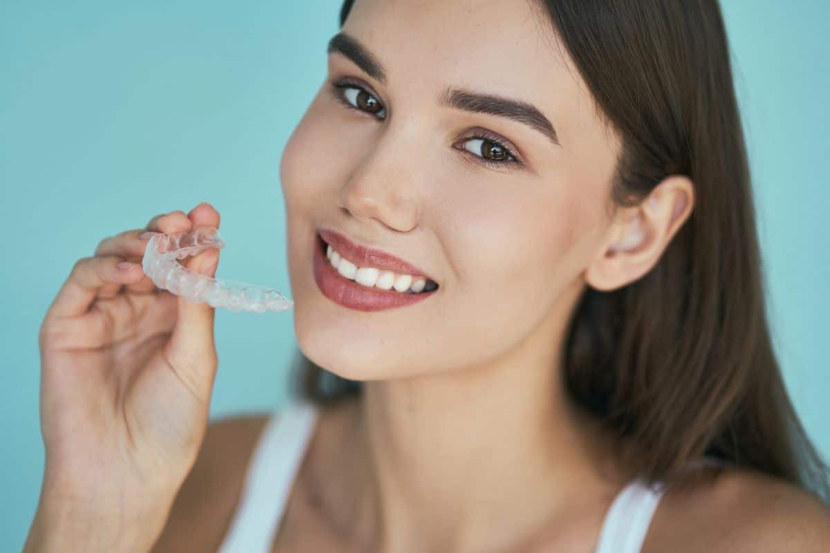 Smiling woman holding clear Invisalign aligner tray against blue background.