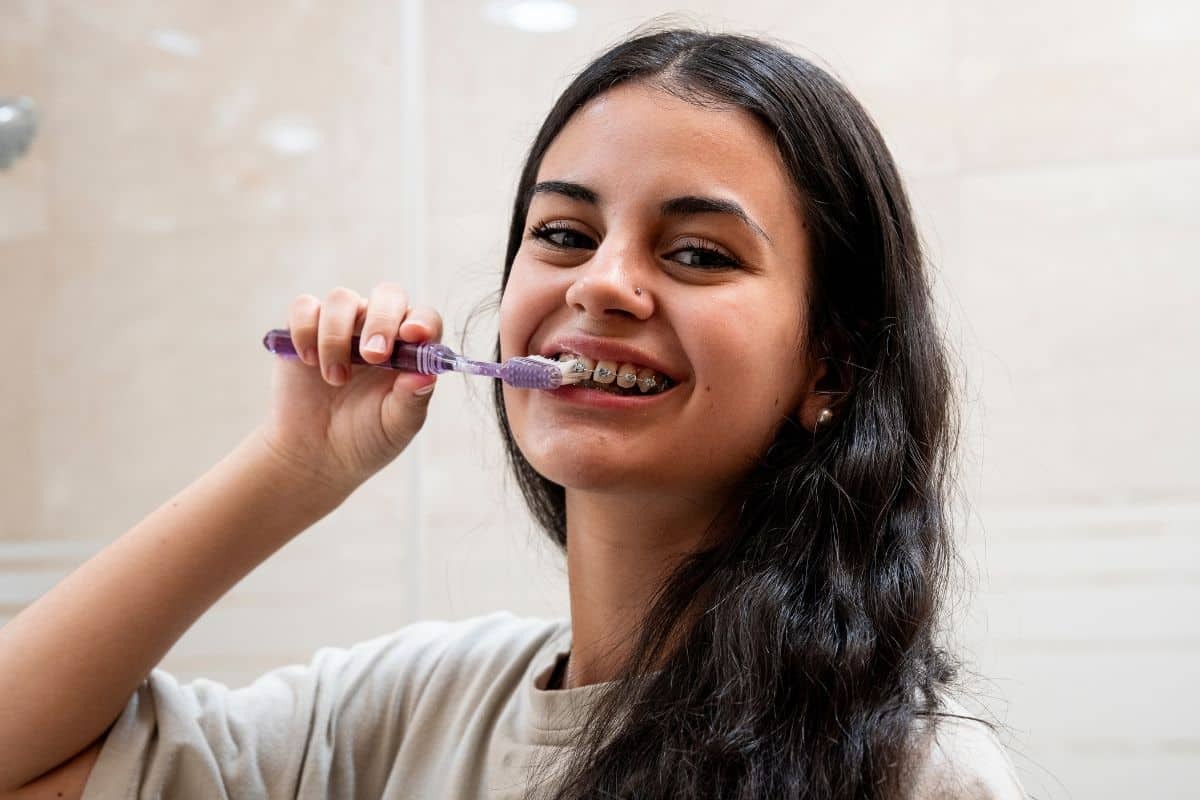 Young woman brushing her teeth while wearing metal braces.