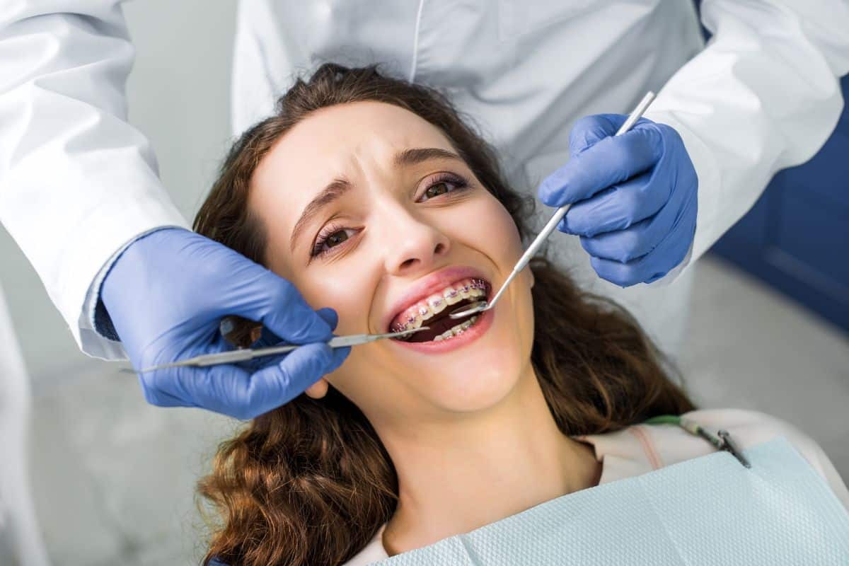 Patient receiving orthodontic examination and treatment with metal braces visible during dental consultation.