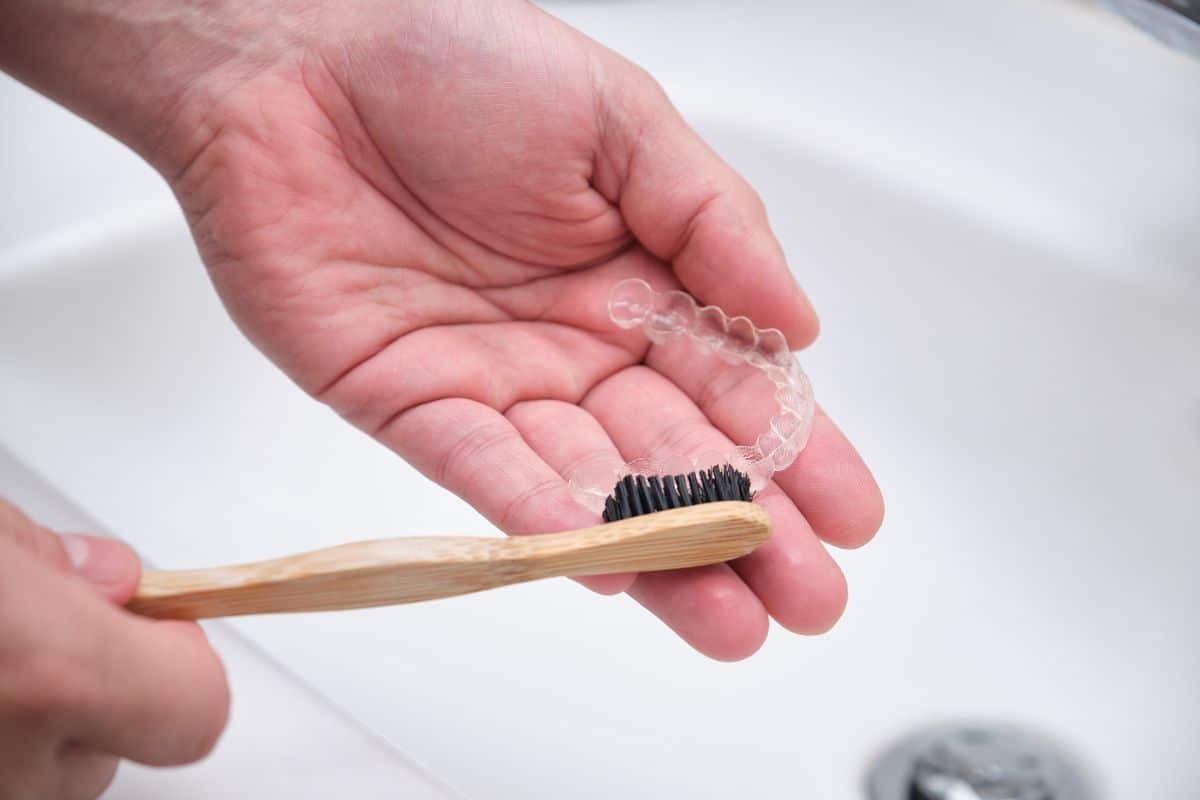 Person holding clear Invisalign aligner and bamboo toothbrush for proper dental hygiene care.