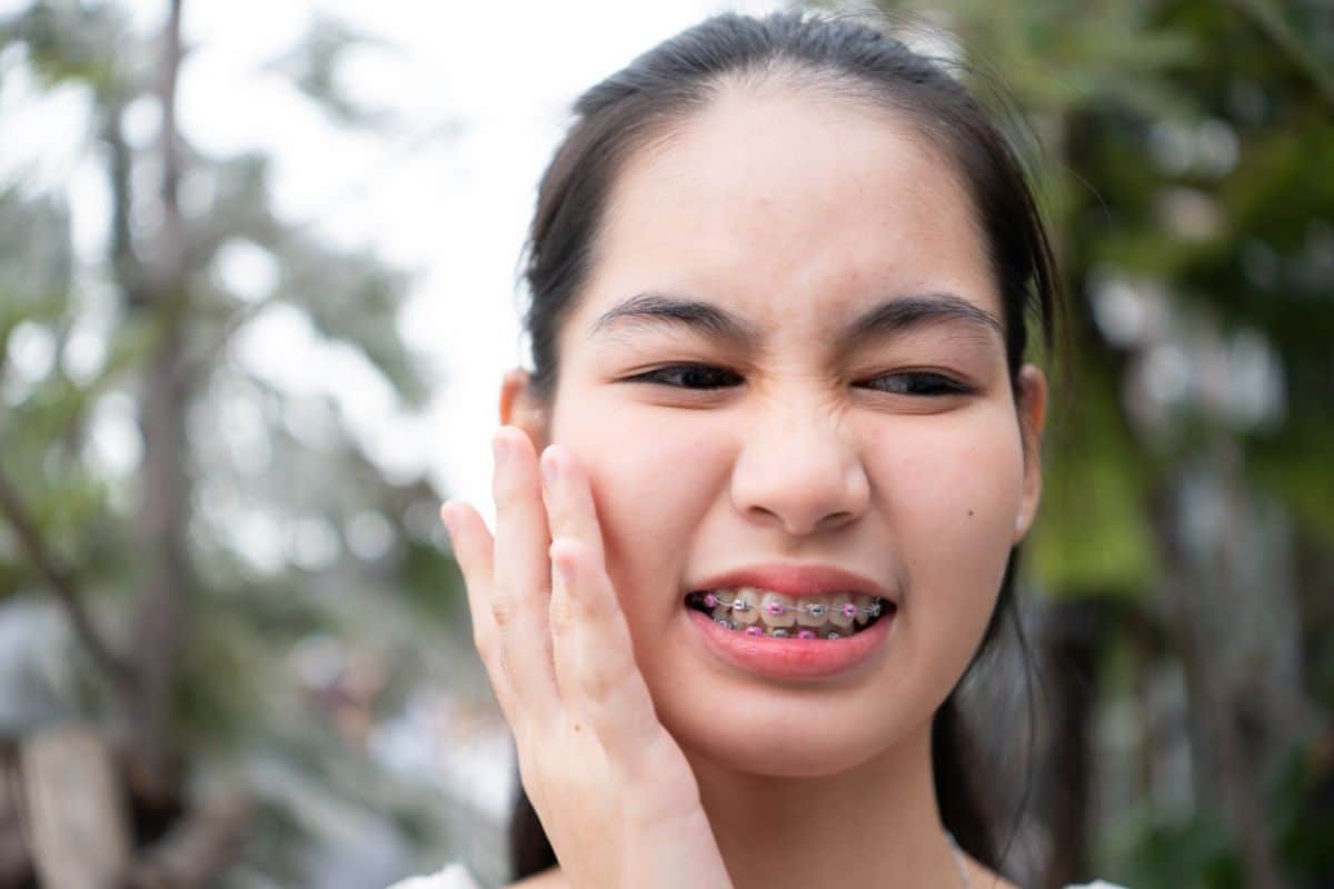 Young woman with braces experiencing tooth discomfort, demonstrating common anterior crossbite symptoms.