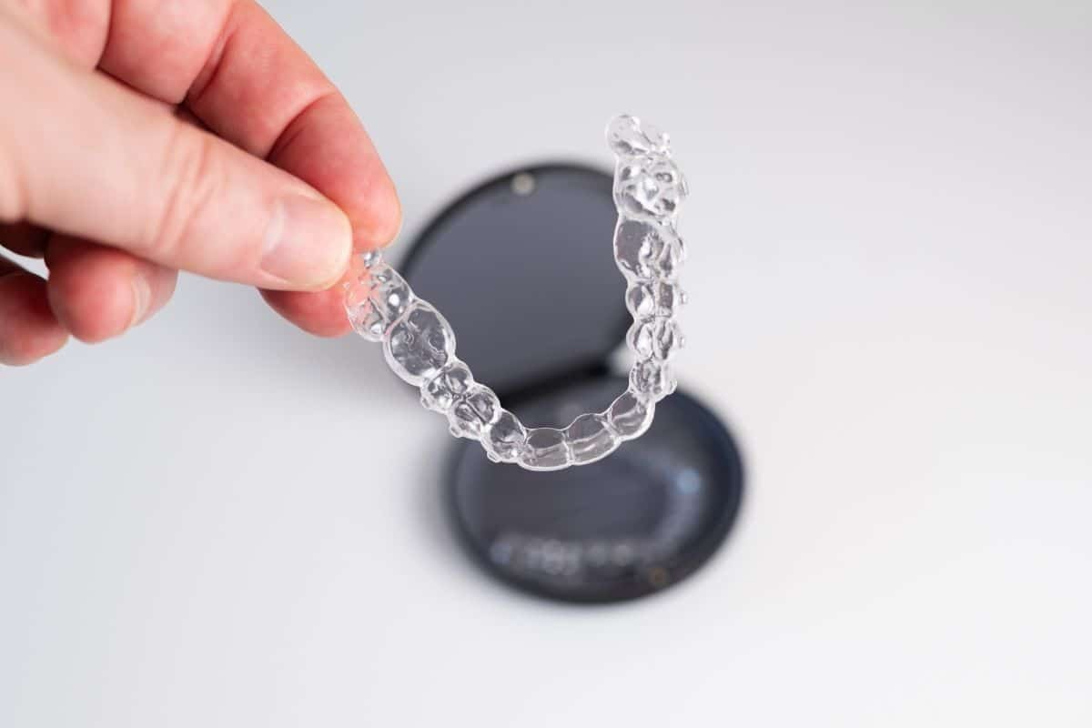 Clear aligner tray held in hand showing transparent orthodontic treatment for smile correction.