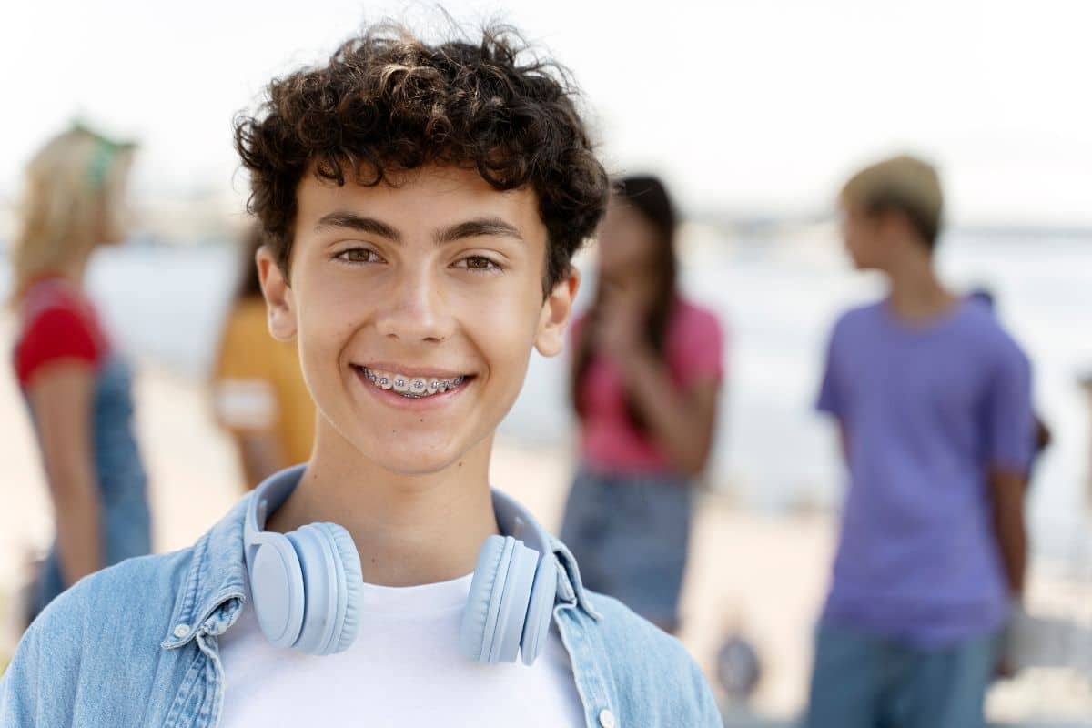 Smiling teenager with braces wearing headphones at the beach with friends.
