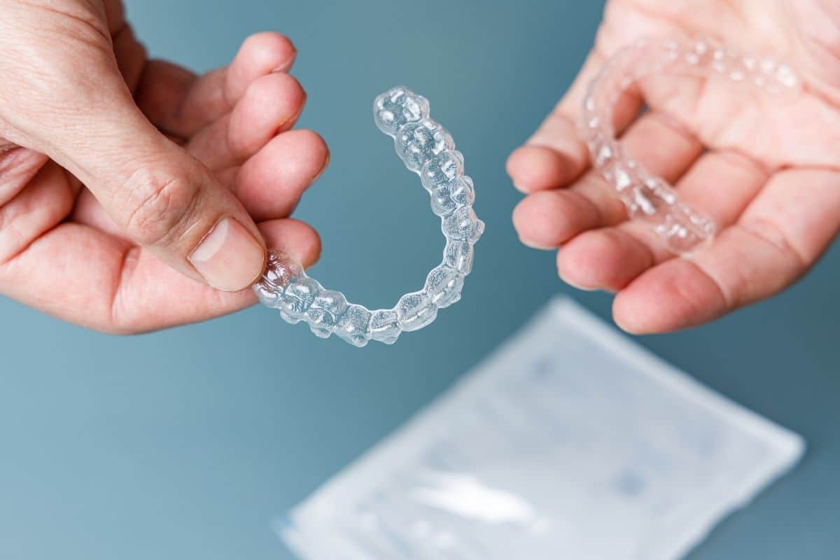 Person holding clear Invisalign aligner showing how treatment corrects crossbite alignment.
