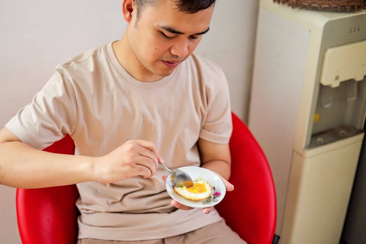 Young man with braces eating soft food from a small plate with a fork.