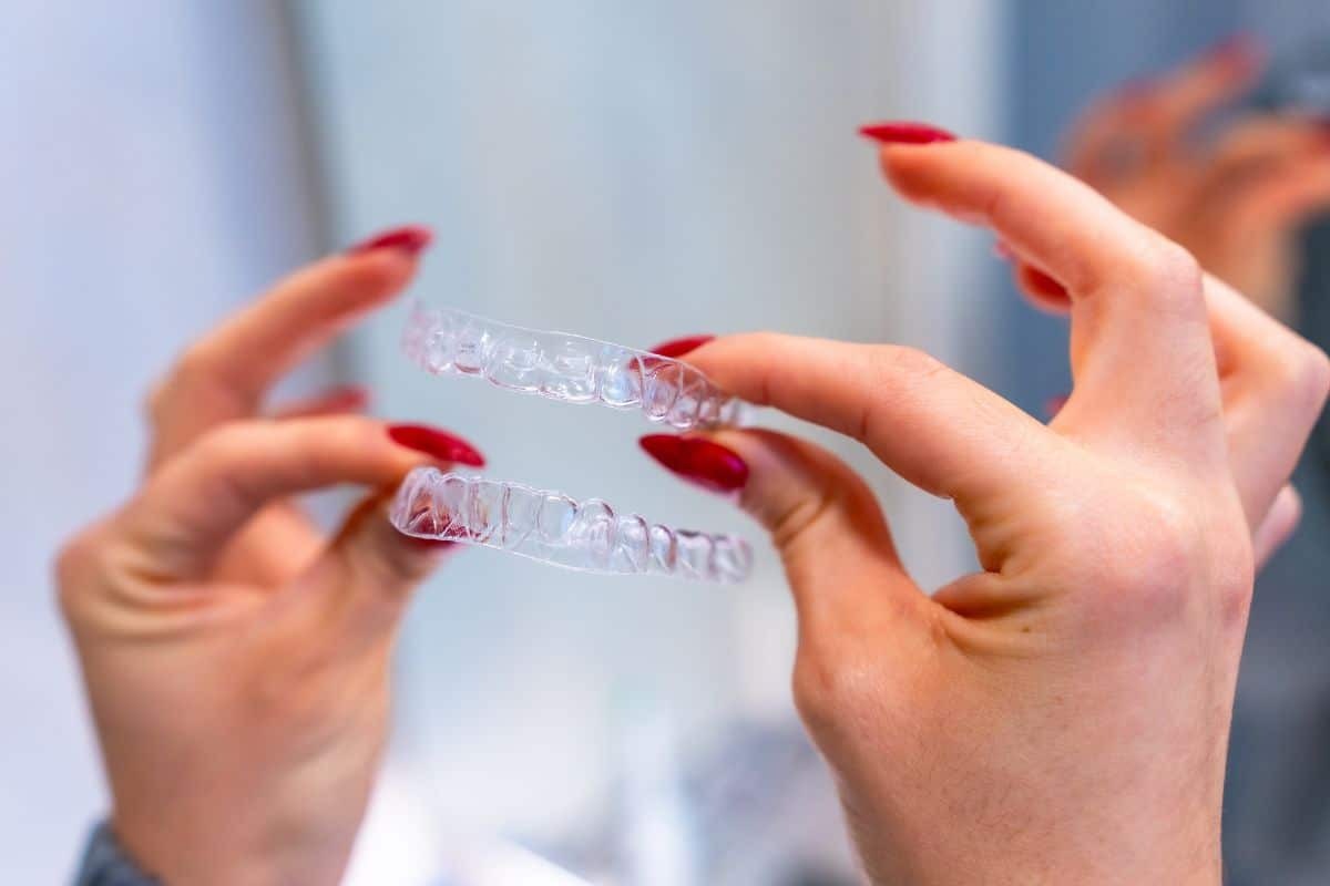 Person holding two clear Invisalign aligners with red nail polish.