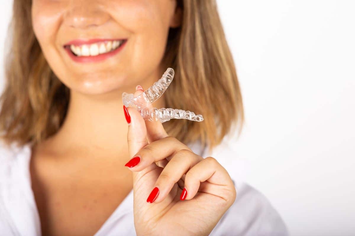 Woman holding clear invisible aligner and smiling, showing orthodontic treatment compliance.