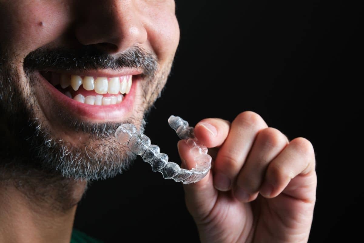 Man smiling while holding clear Invisalign aligner tray for teeth straightening treatment.
