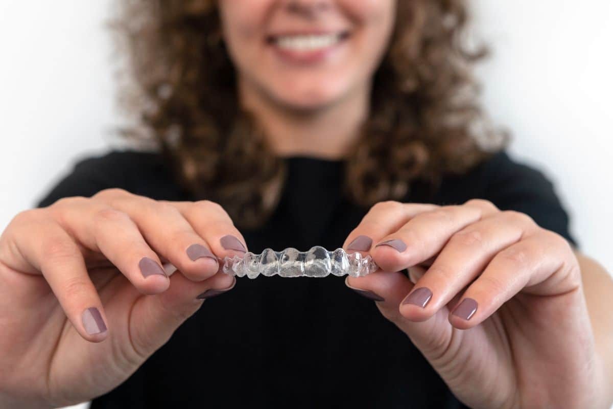Woman holding a clear Invisalign retainer between her hands, smiling.