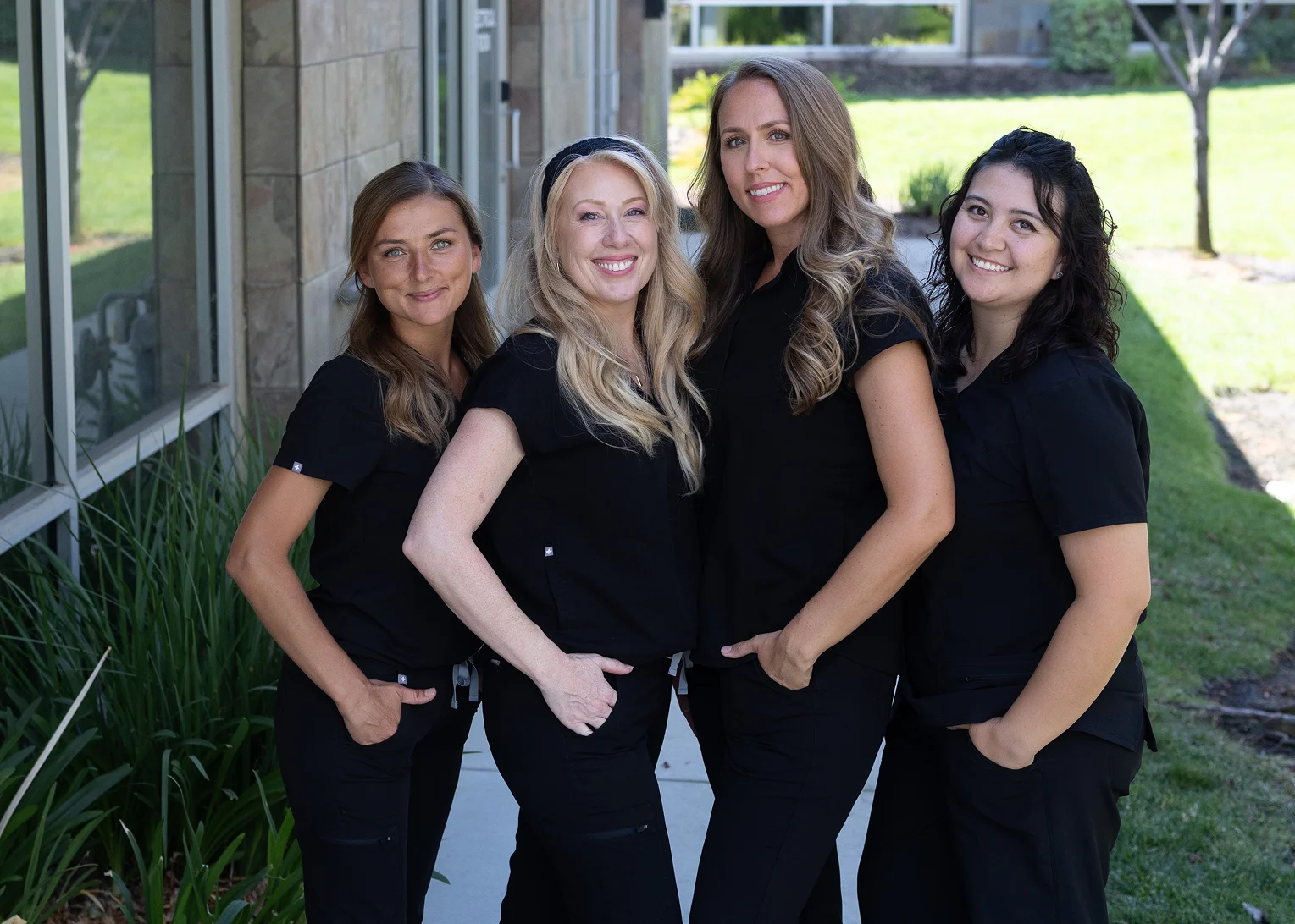Four Dunn Orthodontics staff members in black scrubs smiling together outside the office